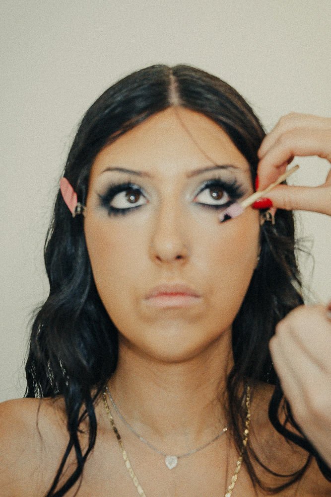 A woman with black hair and editorial makeup having mascara applied by a makeup artist.