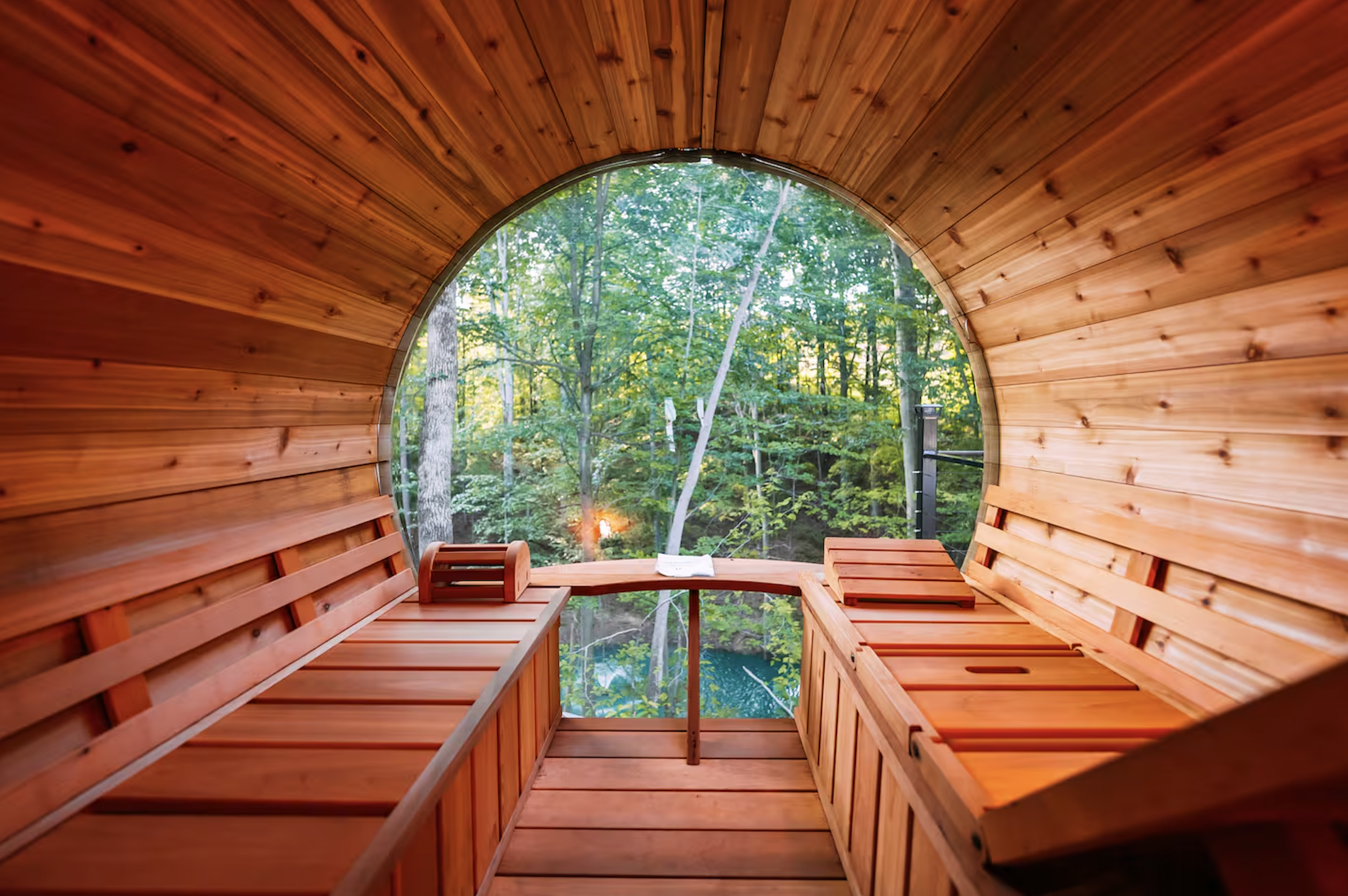 Inside a wooden sauna with a large round window looking out at green trees and forest.