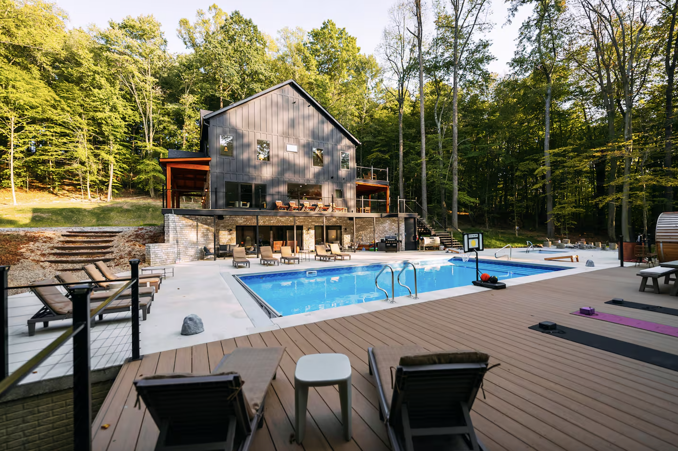 A backyard with a swimming pool, lounge chairs, and a modern house with multiple levels surrounded by trees.