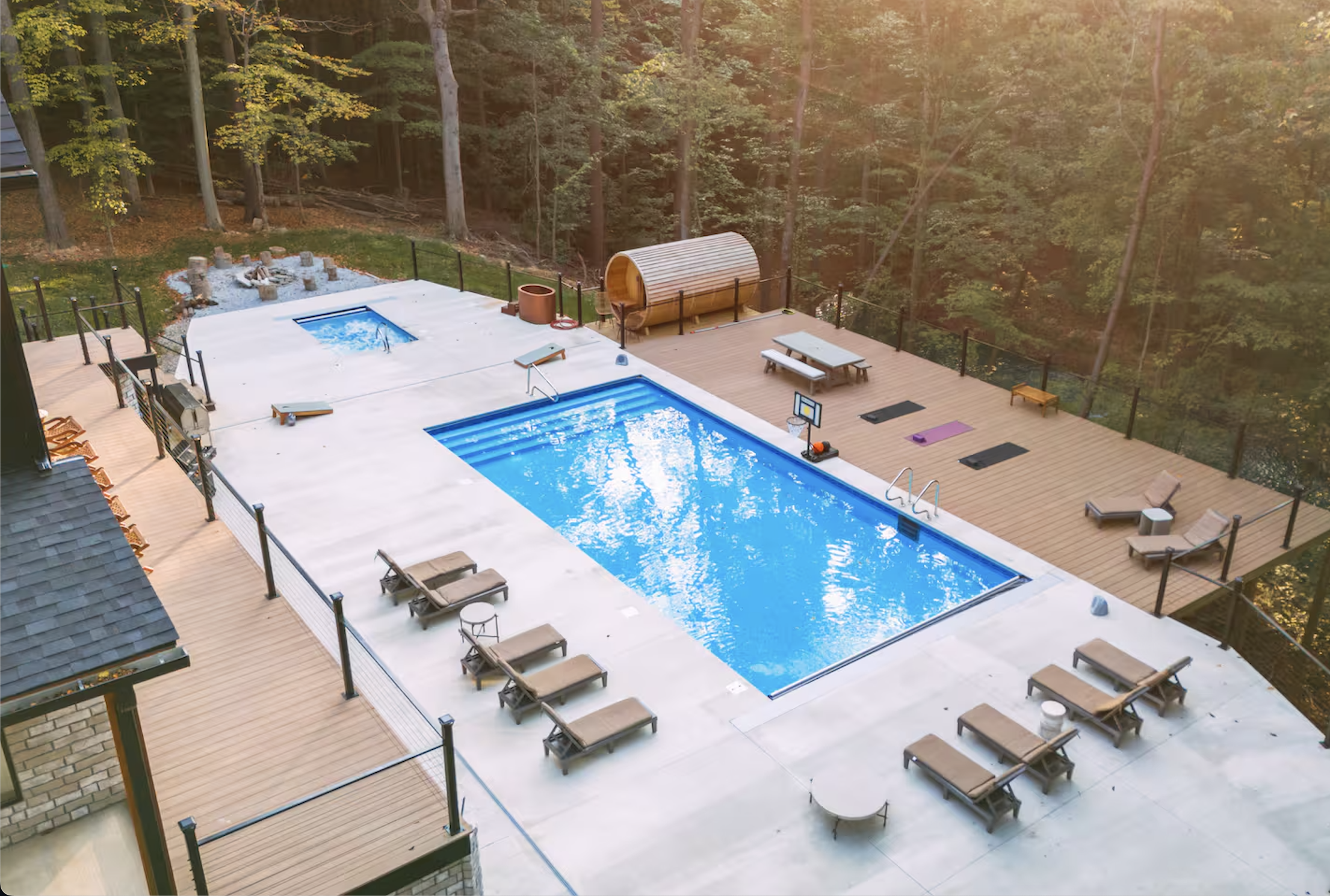 Aerial view of backyard with swimming pool, hot tub, lounge chairs, picnic table, gym equipment, and wooded forest surroundings.