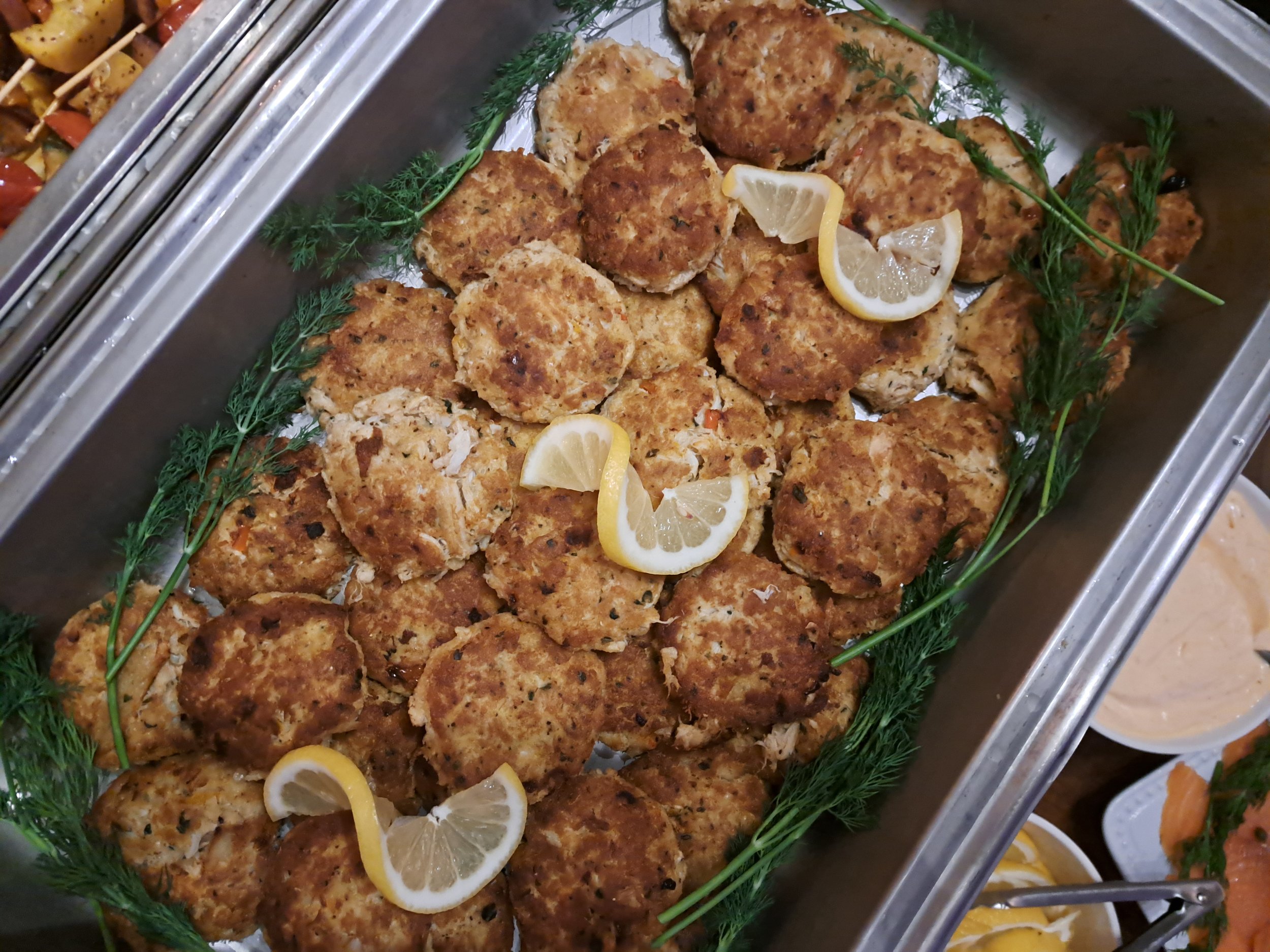 Tray of crab cakes garnished with lemon wedges and fresh herbs.