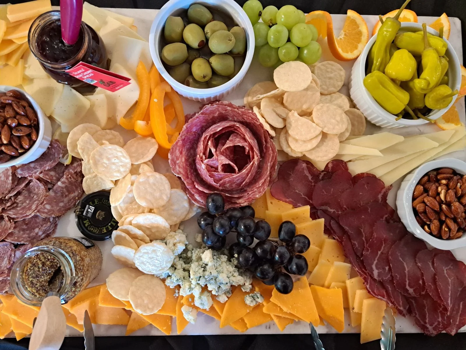 A charcuterie board with various cheeses, cured meats, olives, grapes, crackers, nuts, and fruit slices for serving.