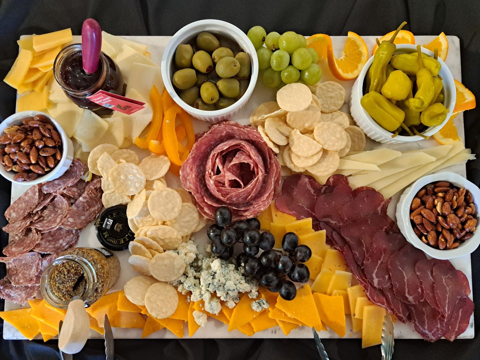 A charcuterie board with various cheeses, cured meats, olives, grapes, crackers, nuts, and fruit slices for serving.