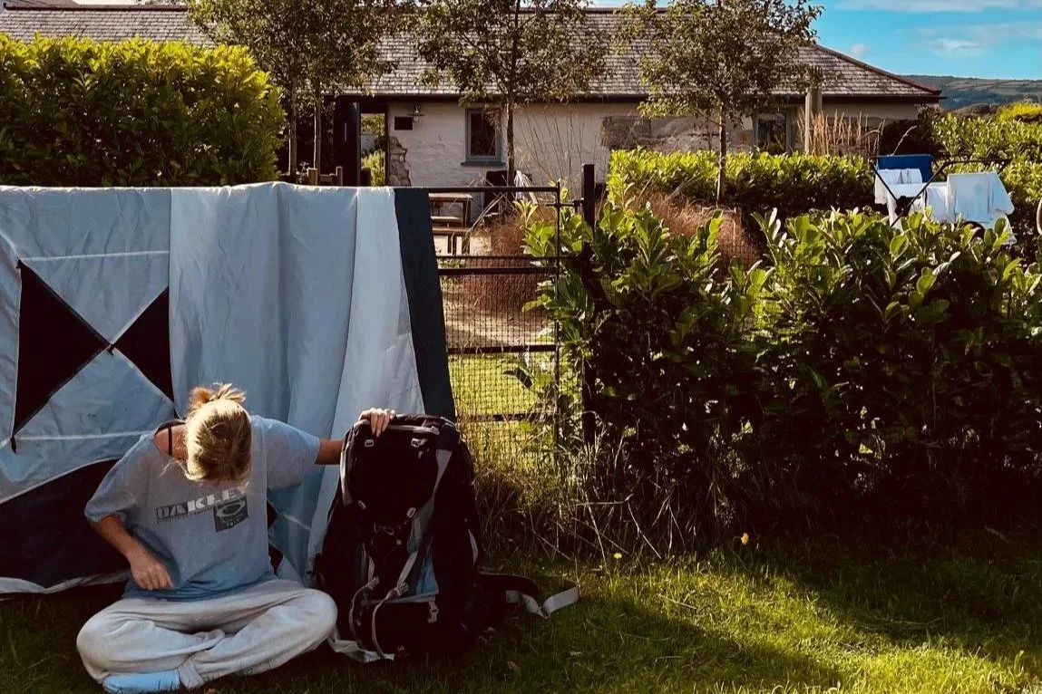 Tired teenager sitting by a hedge outside a luxury cottage in Cornwall after Boardmasters