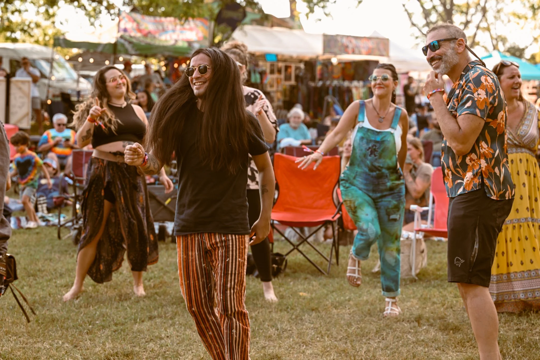 People enjoying music and dancing at an outdoor festival with vendor tents in the background.