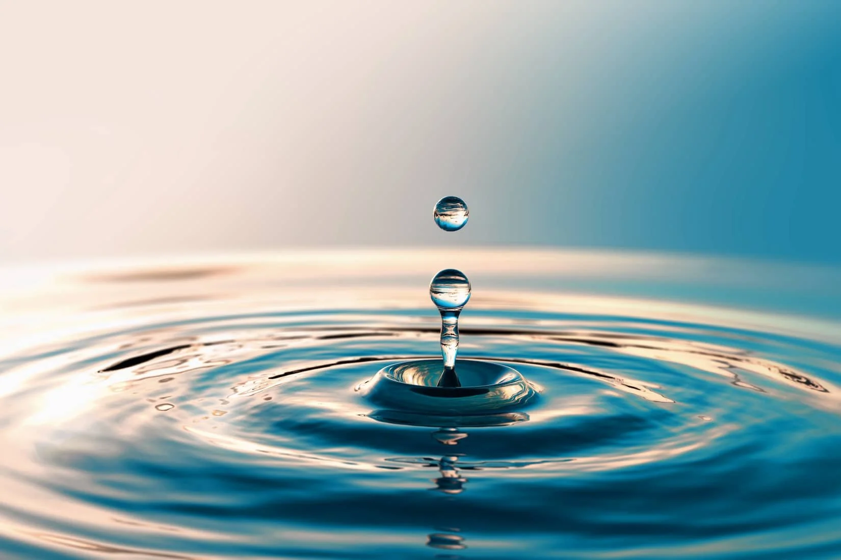 Wassertropfen erzeugt Wellen auf ruhiger Wasseroberfläche. Symbolbild für das Resilienz-Retreat in der Villa Lux im Rheingau, September 2026.