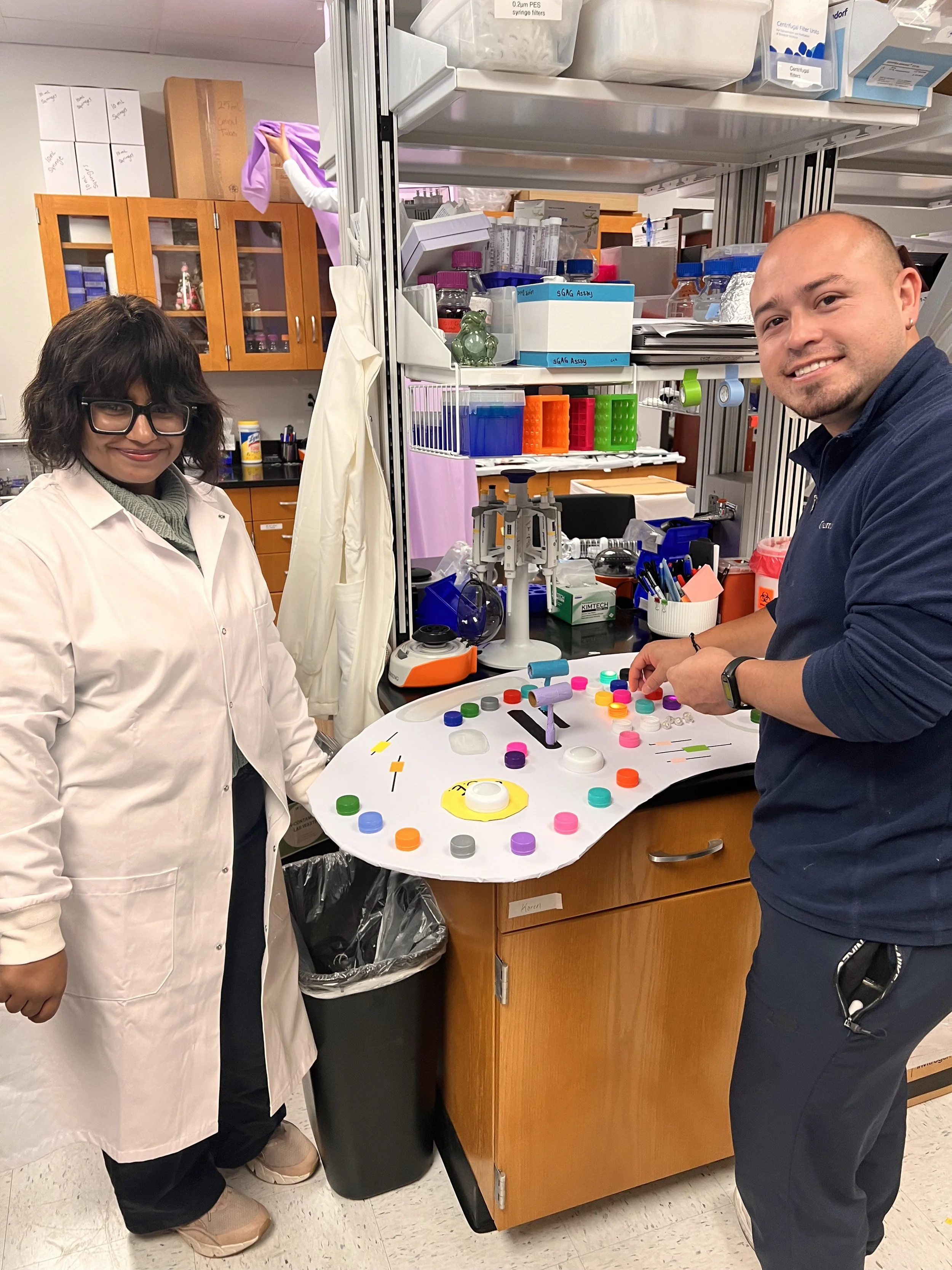Two researchers in the lab standing beside a colorful hands-on science project.