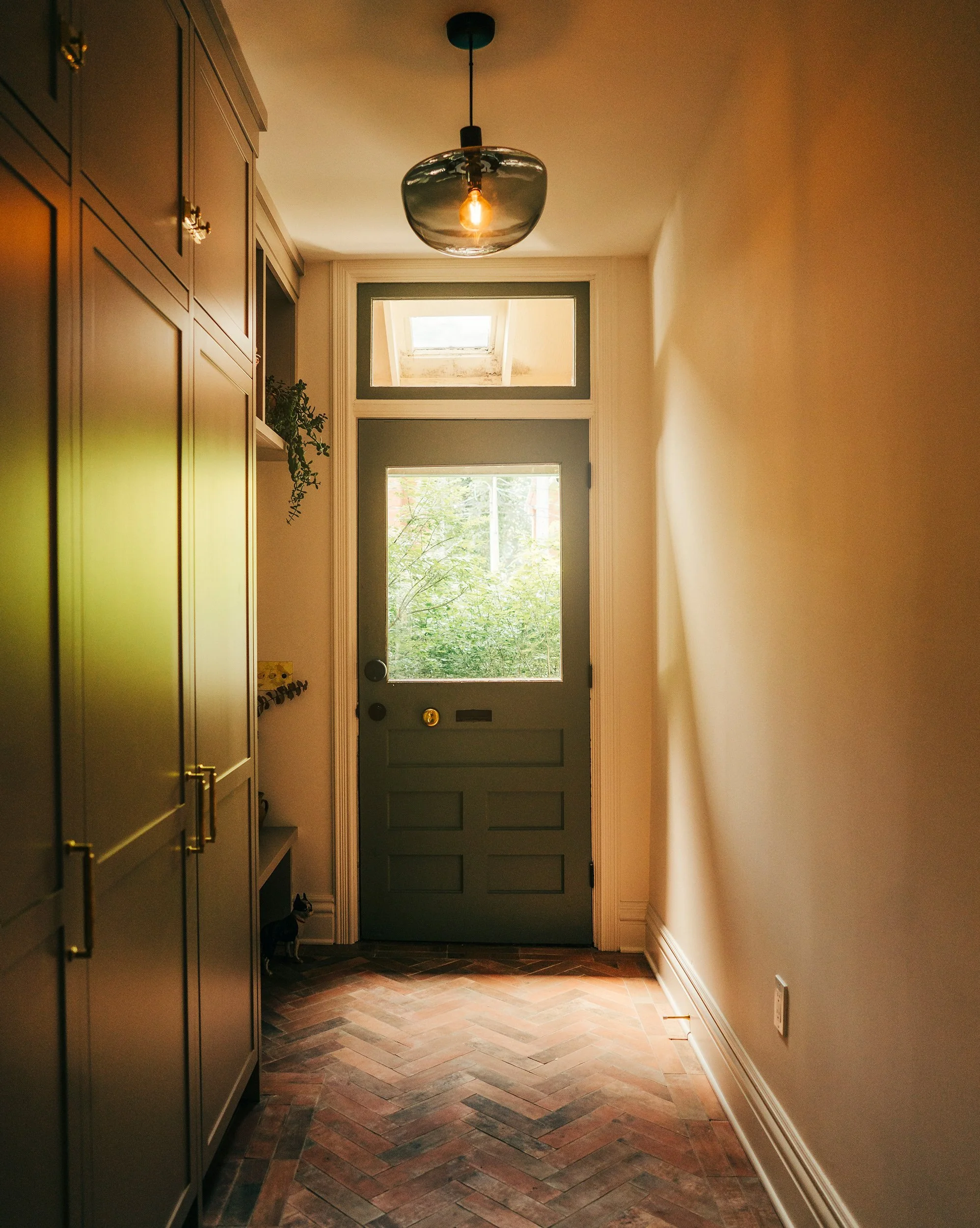 Interior view of a hallway with a blue front door, a ceiling light fixture, and wooden herringbone-patterned flooring.