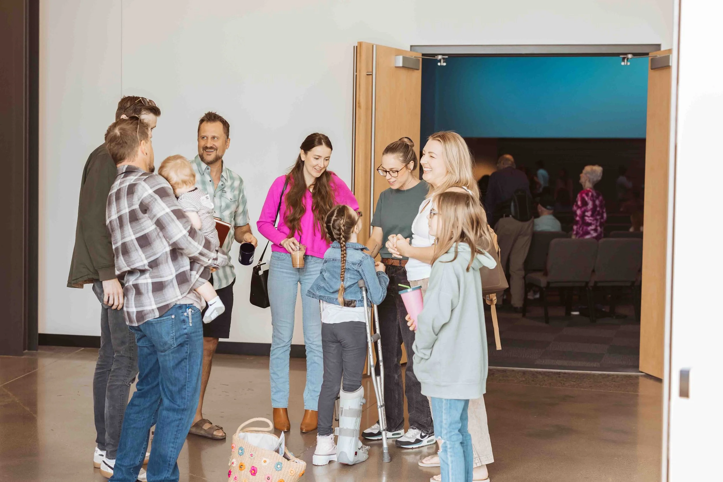 Group of people, including children and adults, gathered in a hallway outside a room, waiting in line for a presentation or event.