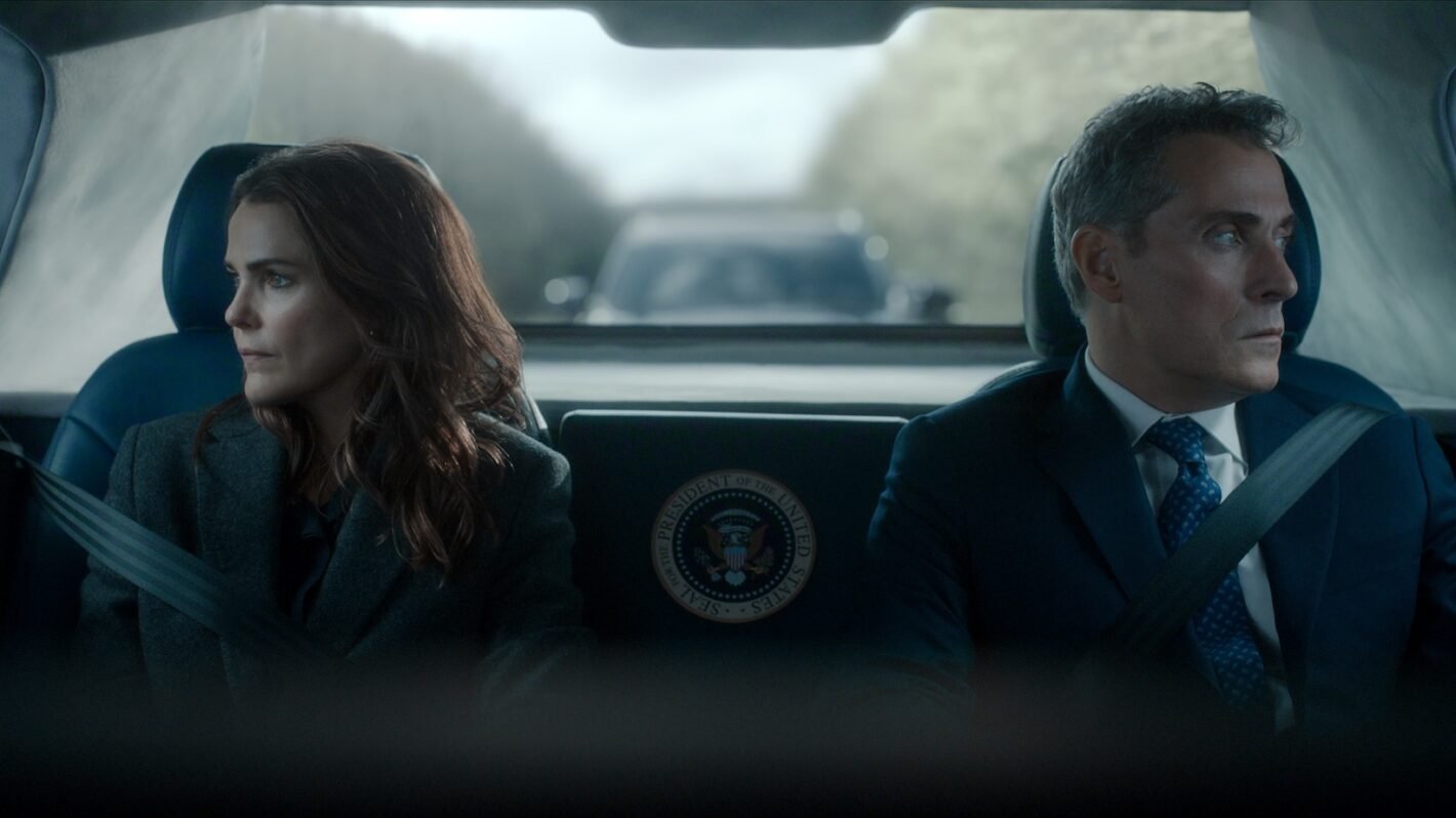 A woman looks out the left window as a man looks out the right window of the backseat of an SUV