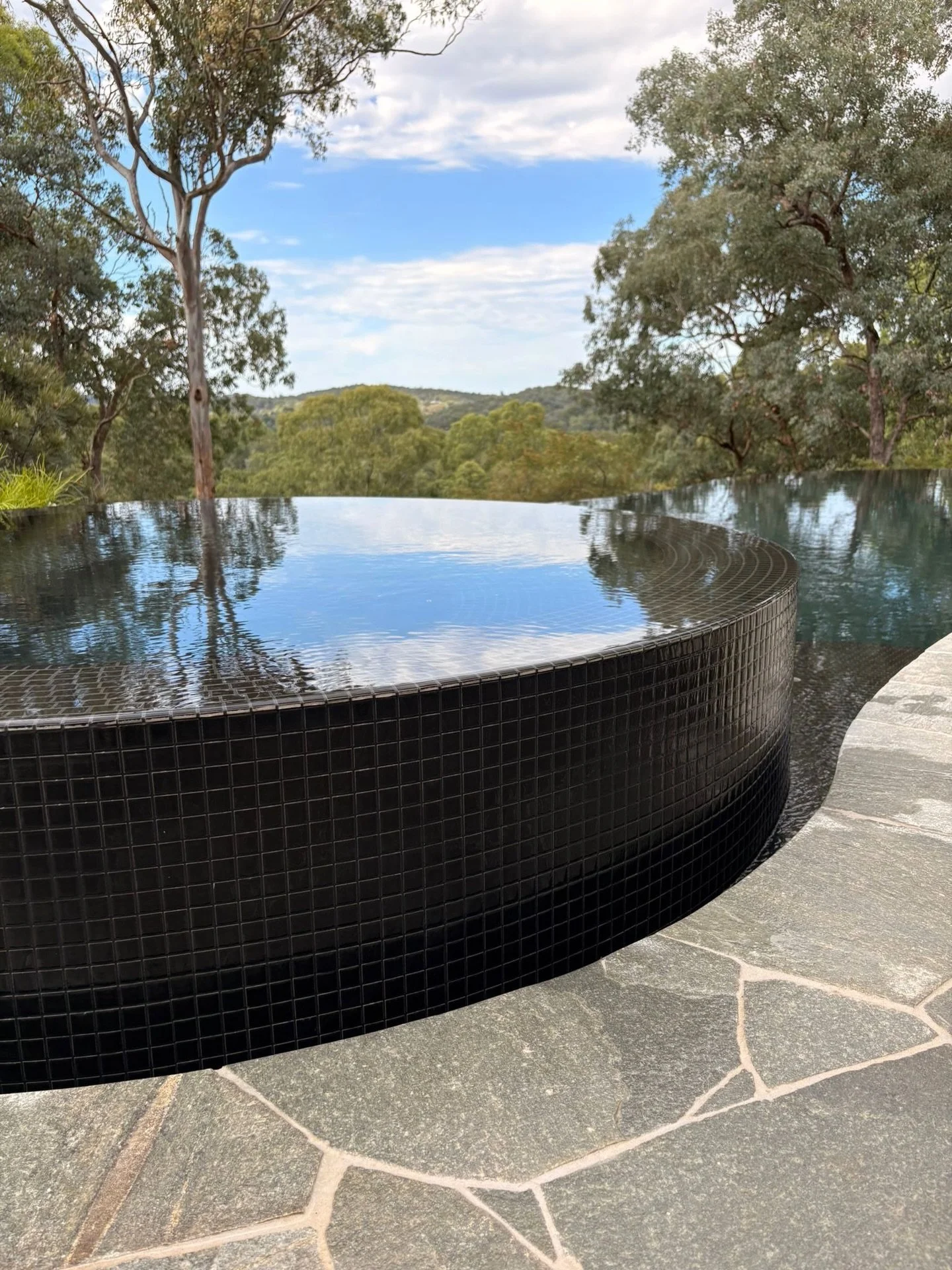This one speaks for itself.

A curved, negative-edge pool just handed over, opening directly to the treetops beyond. Dark mosaic tiles deepen the water&rsquo;s tone, while the seamless edge allows the landscape to lead.

Quietly dramatic and built to