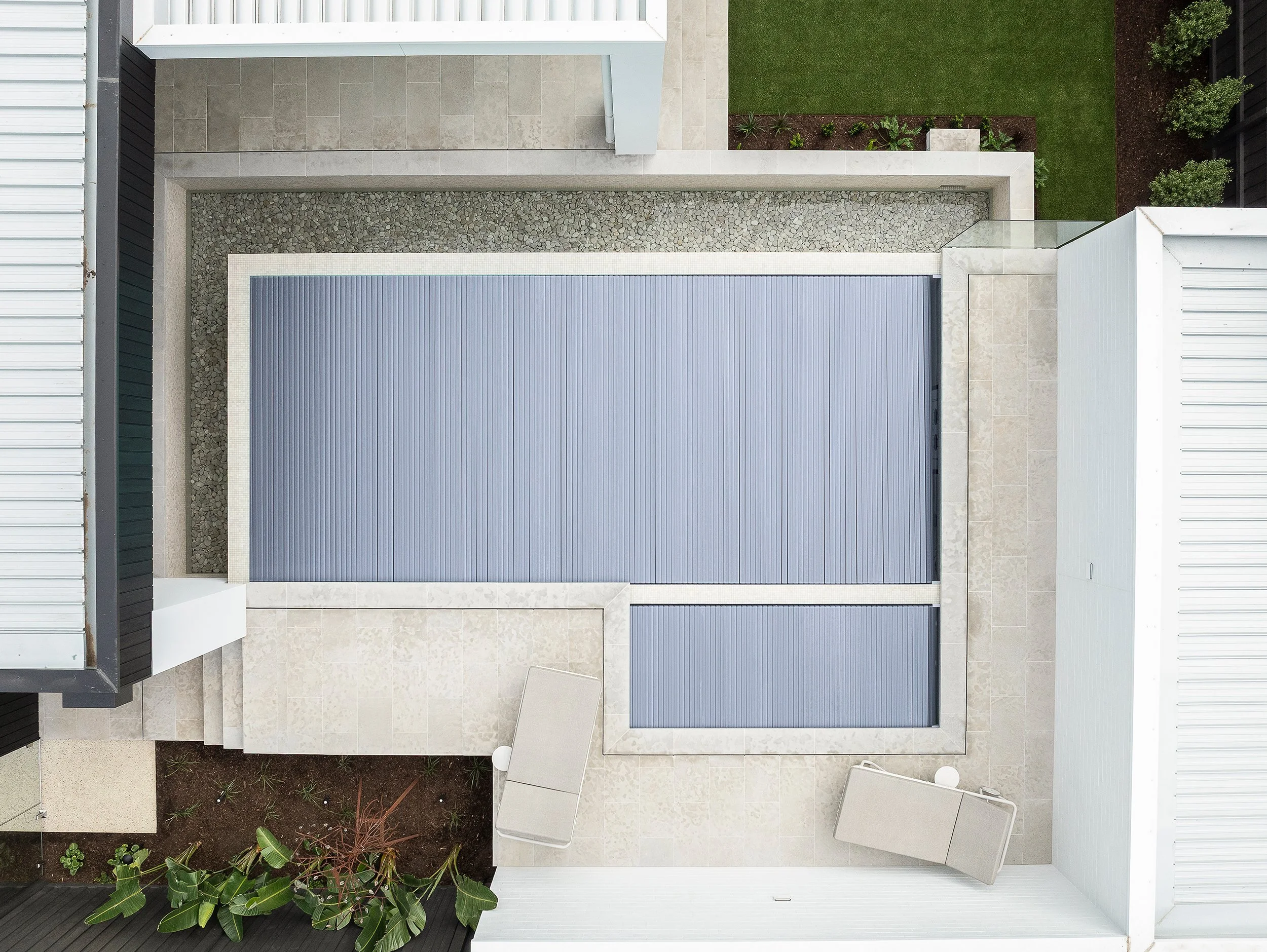 Top-down view of a modern house backyard with a large blue retractable glass roof, landscaped garden, and lounge chairs.