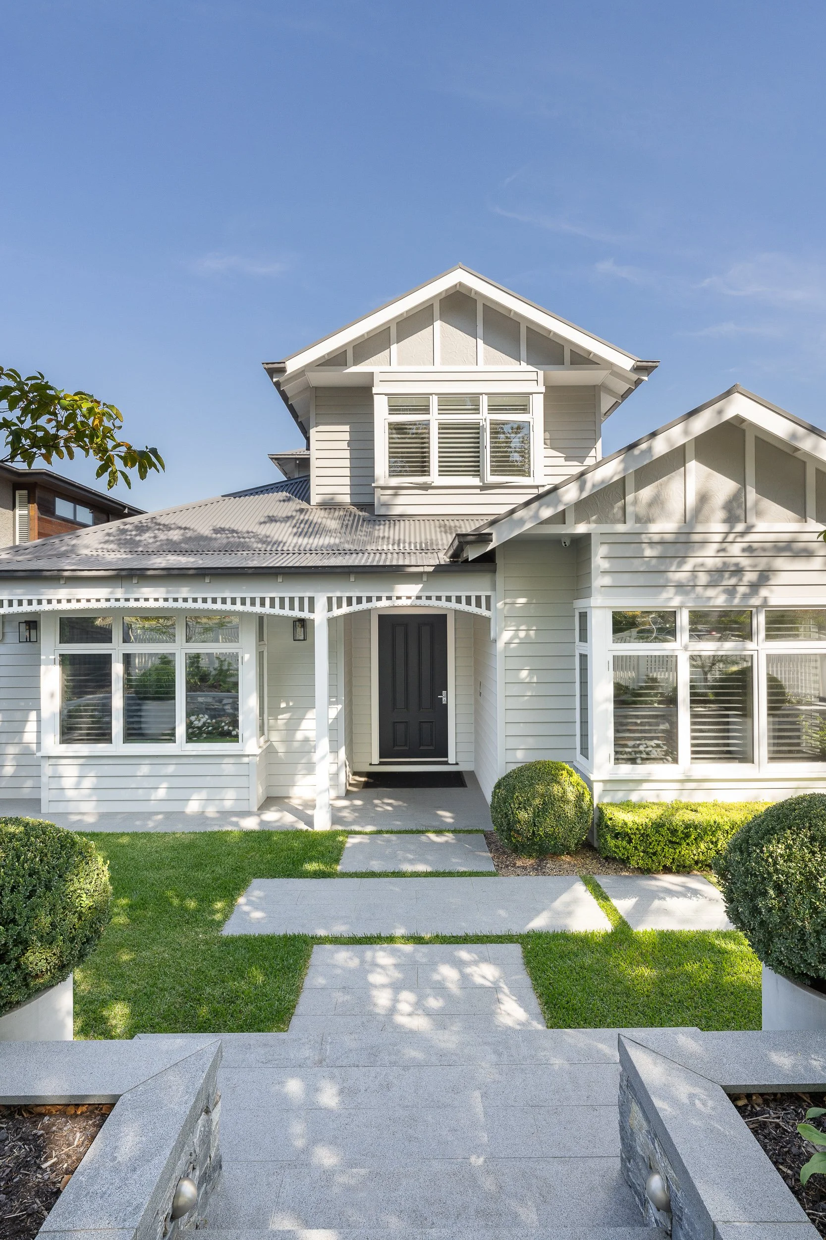 Front view of a modern white house with stairs, bushes, and clear windows under a blue sky.