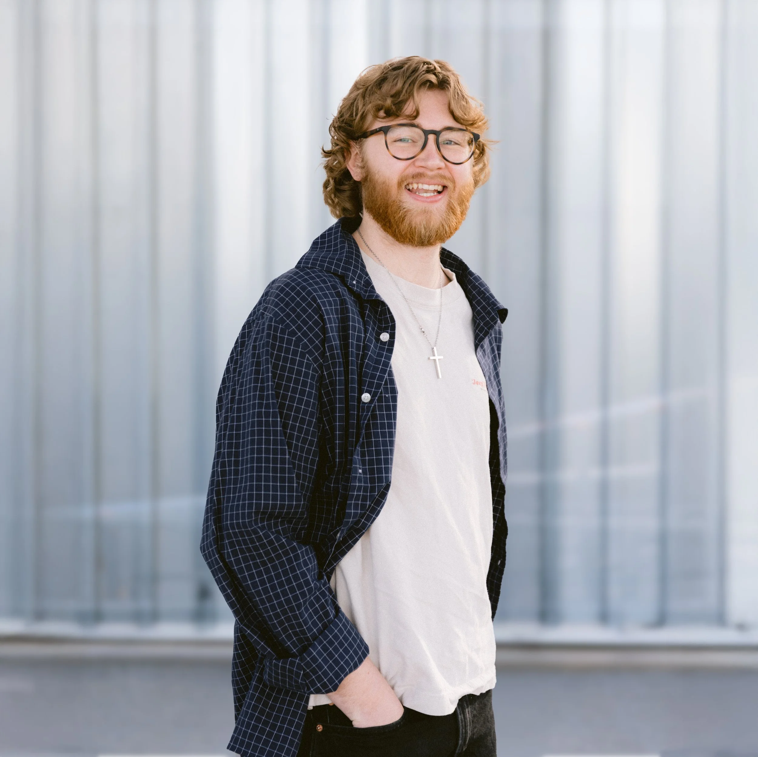 A smiling man with glasses and a beard standing inside a bright, modern greenhouse with glass walls.