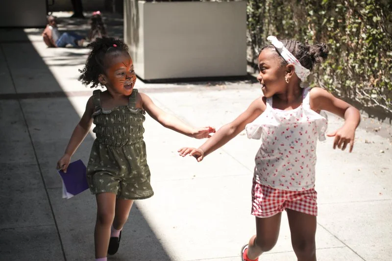 Two young girls happily holding hands and running together outdoors on a sunny day.