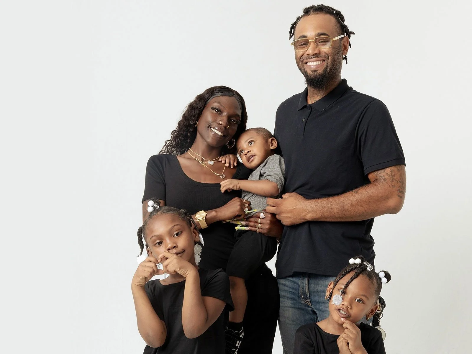 A happy multi-racial family portrait with a mother, father, and three young daughters, all smiling and dressed casually against a plain white background.
