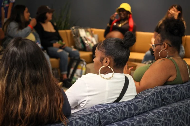 Group of diverse women sitting on couches in a lounge, engaging in conversation.