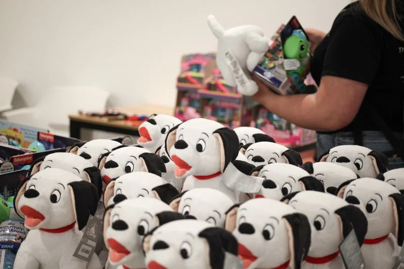 A display of plush Dalmatian dog toys on a table with a person holding a toy and a box of toys in the background.
