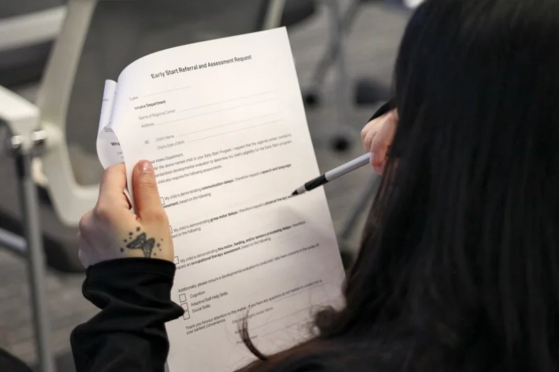 Person holding a form titled 'Early Start Referral and Assessment Request' and using a pointer or pen to read it.
