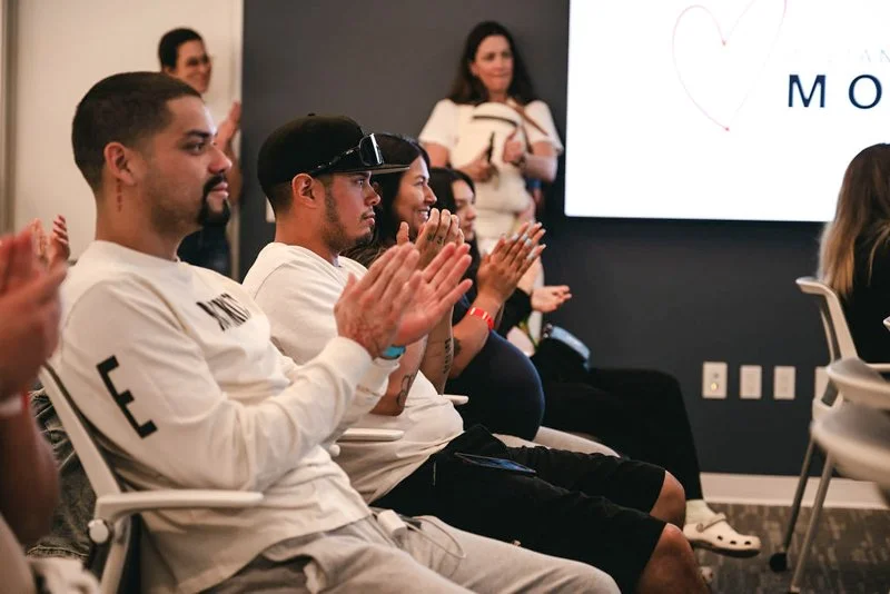 People sitting and clapping at a presentation or event in a conference room.