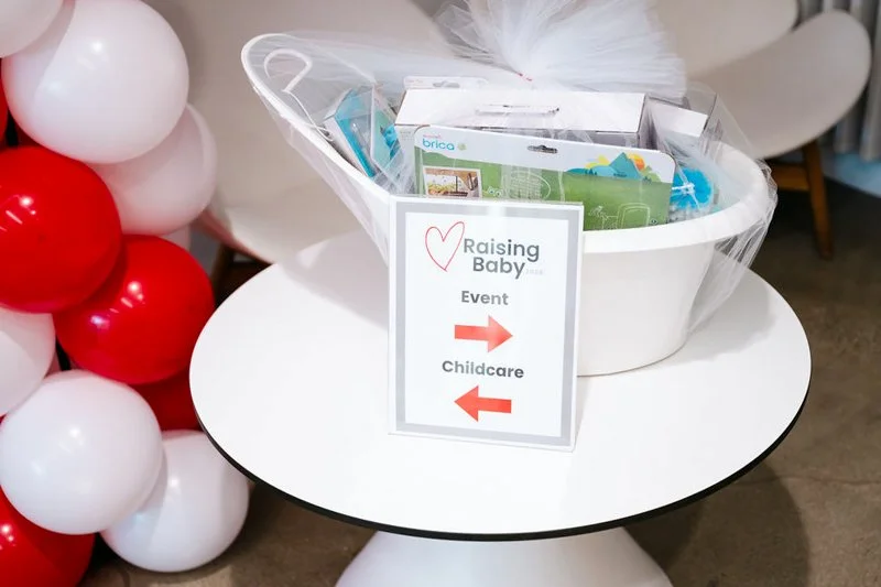 Sign on a table indicating directions for 'Raising Baby' event, with arrows pointing right for 'Event' and left for 'Childcare'