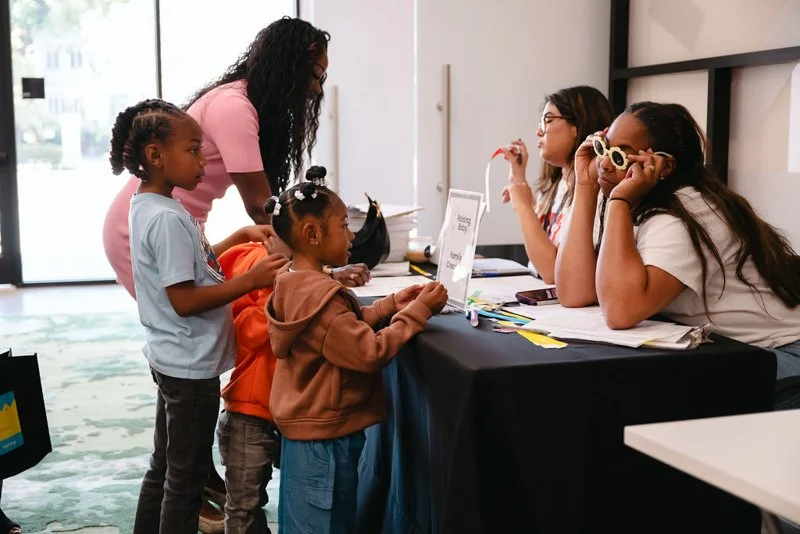 Children at a check-in table talking to two women sitting behind the table.