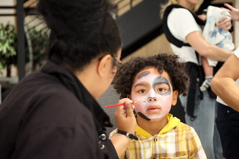 A young boy with face paint resembling a panda is getting ready for a costume or face painting event.