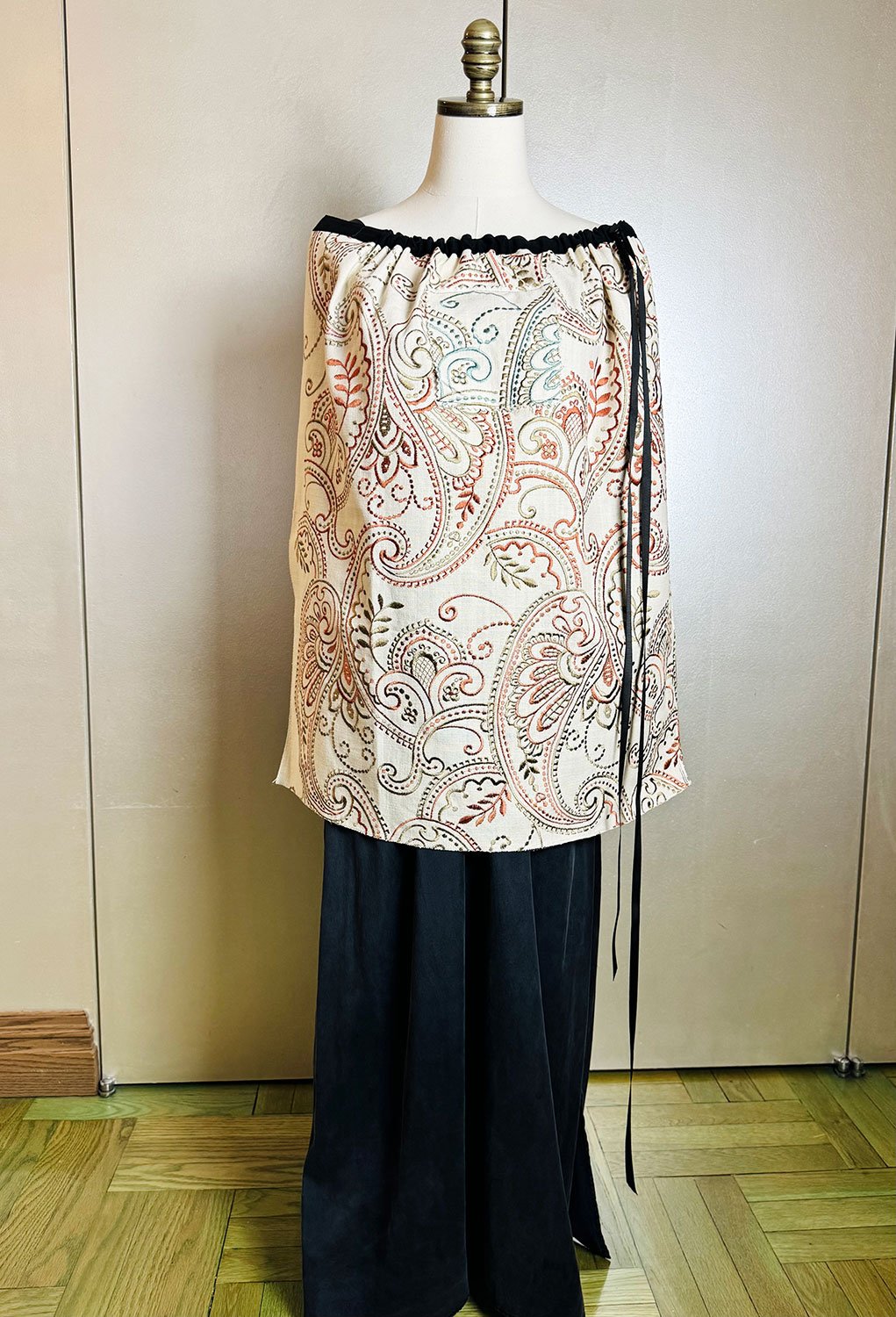 Piper overskirt on mannequin shown as cape with hoodie pocket and ribbon bow