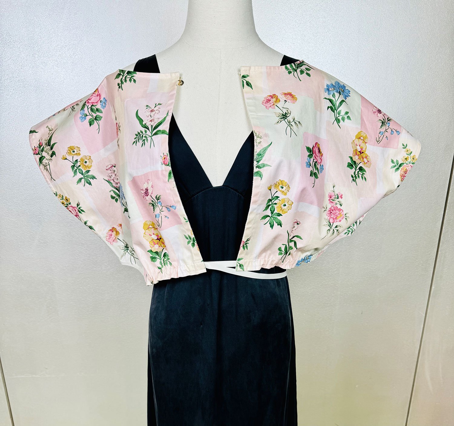 Frida Capelet worn reversed pink coated chintz print on mannequin shown worn open front view with gros grain ribbon adjustable wrap