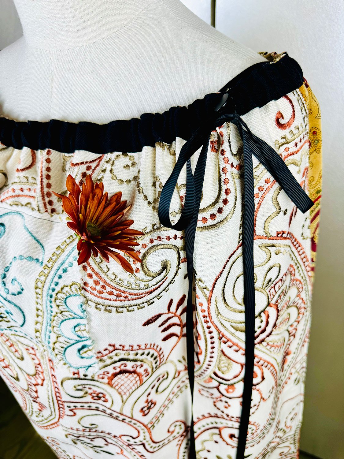 Piper overskirt on mannequin shown as cape with hoodie pocket with flower and ribbon bow