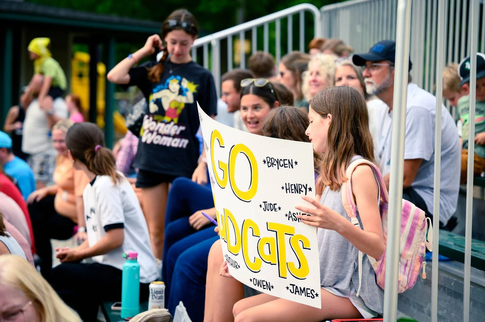 Crowd sits on metal bleachers cheering on their favorite little leaguers.