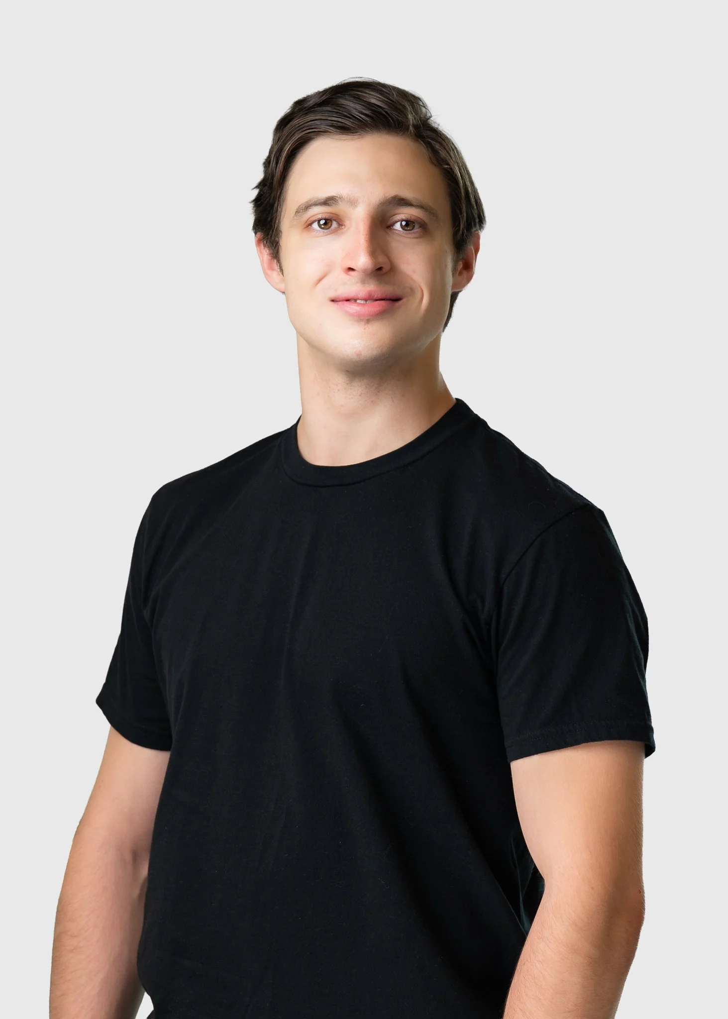 A young man with brown hair wearing a black t-shirt, standing against a light gray background.