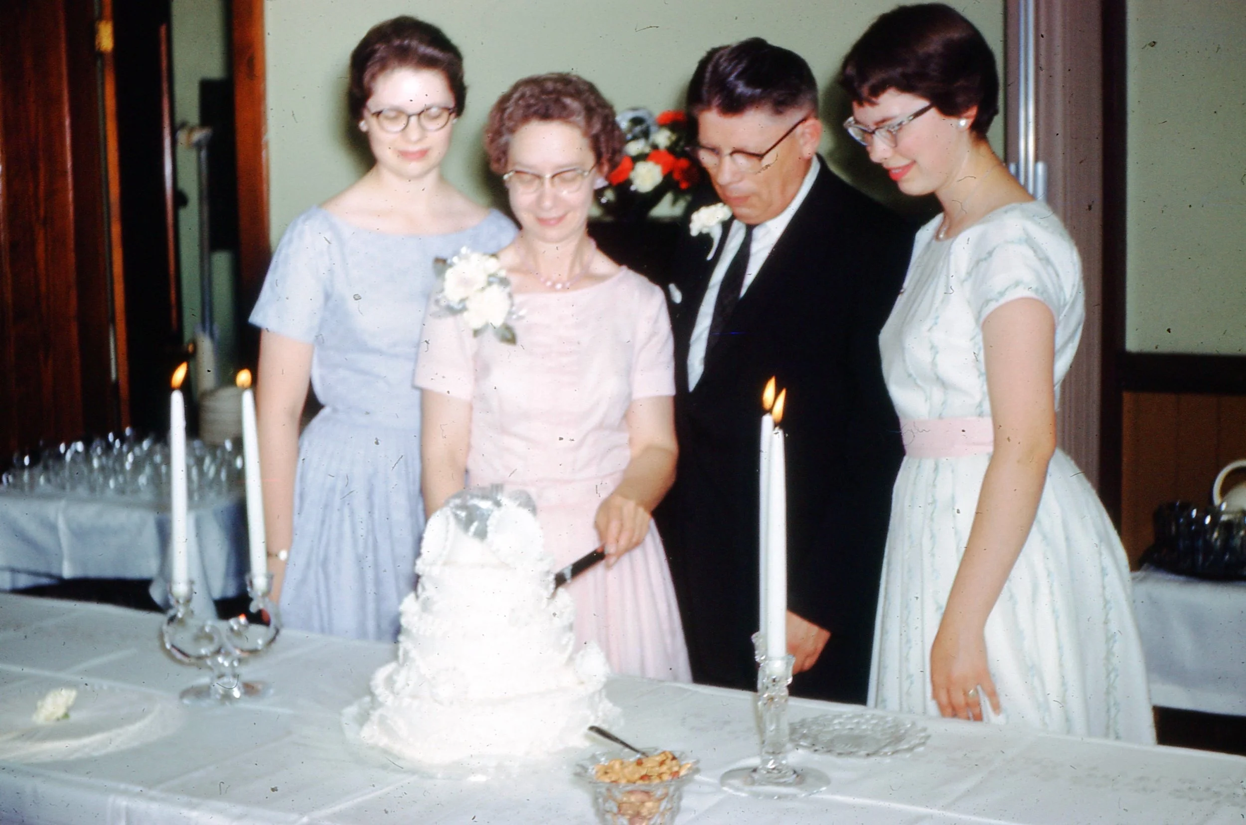 Family gathered around a wedding cake, with candles lit, at a wedding celebration.