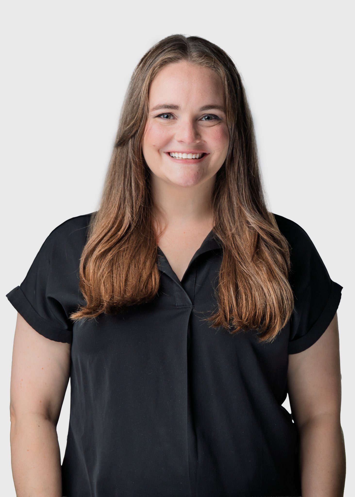 Portrait of a woman with long brown hair wearing a black shirt, smiling, against a plain light grey background.