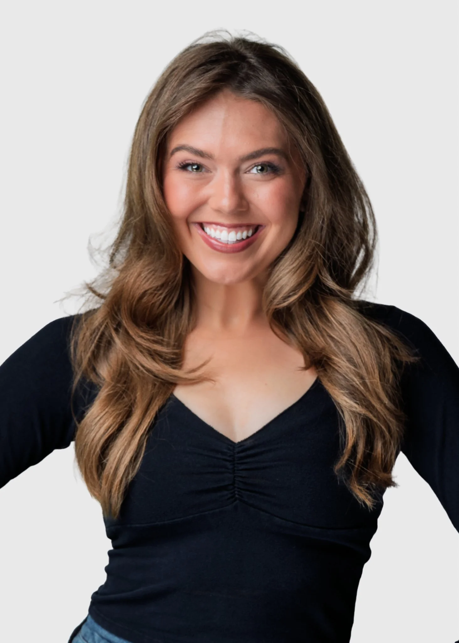 Portrait of a woman with long wavy brown hair, smiling, wearing a black top, against a plain light gray background.