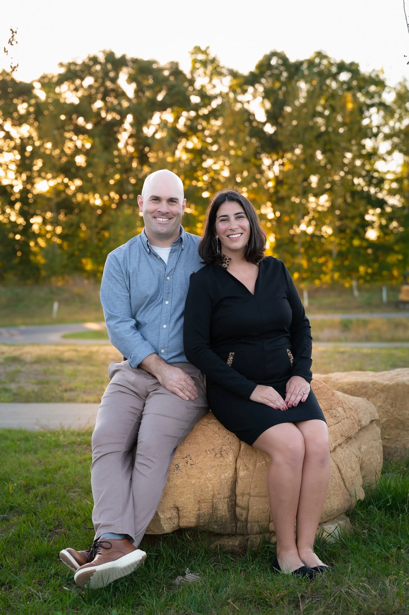 Parents sitting together on a large rock with sunlit trees behind them at Carpenter Nature Preserve