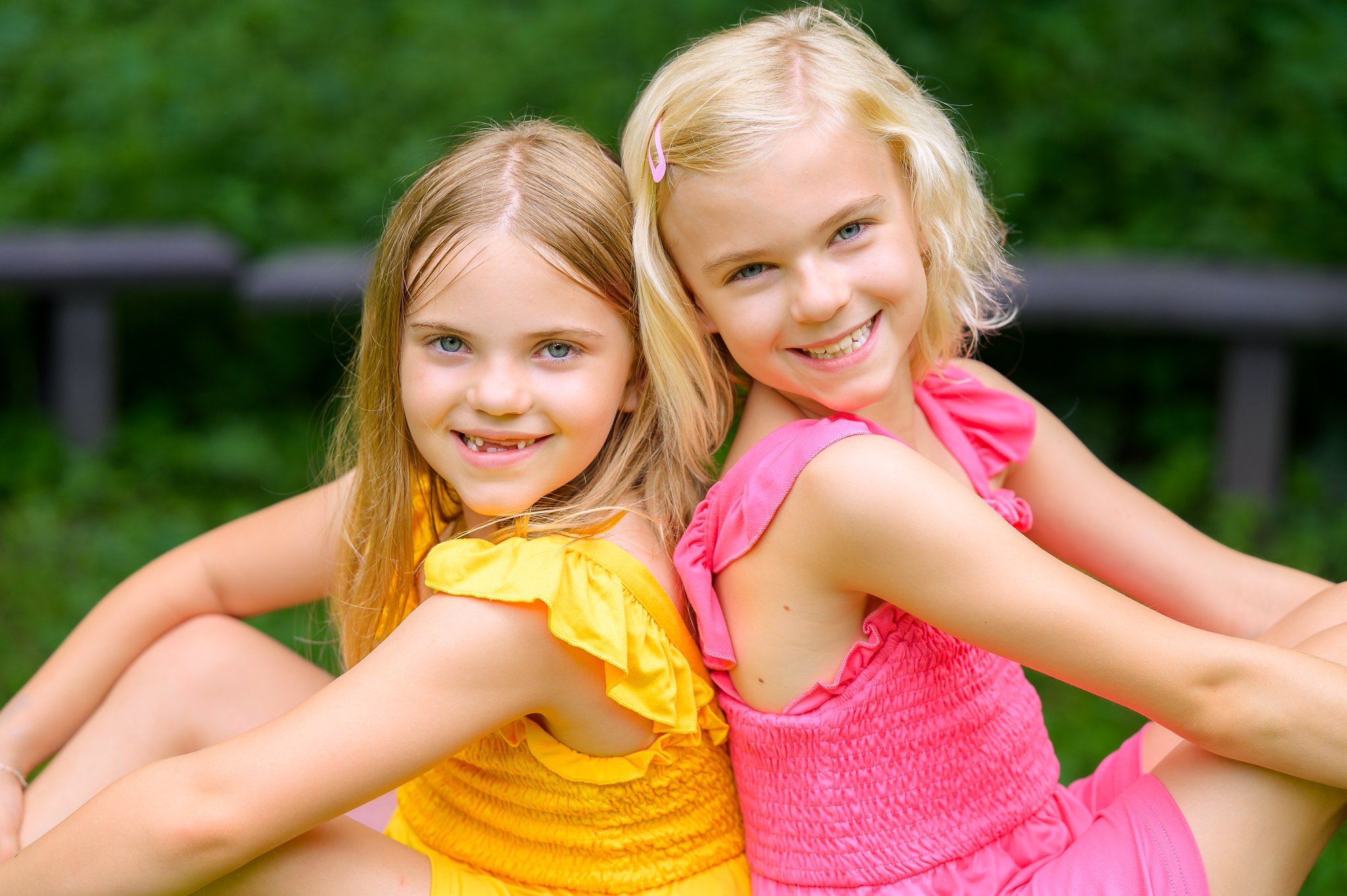 Two little girls in colorful dresses happily sitting together on a bench, enjoying their time outdoors.
