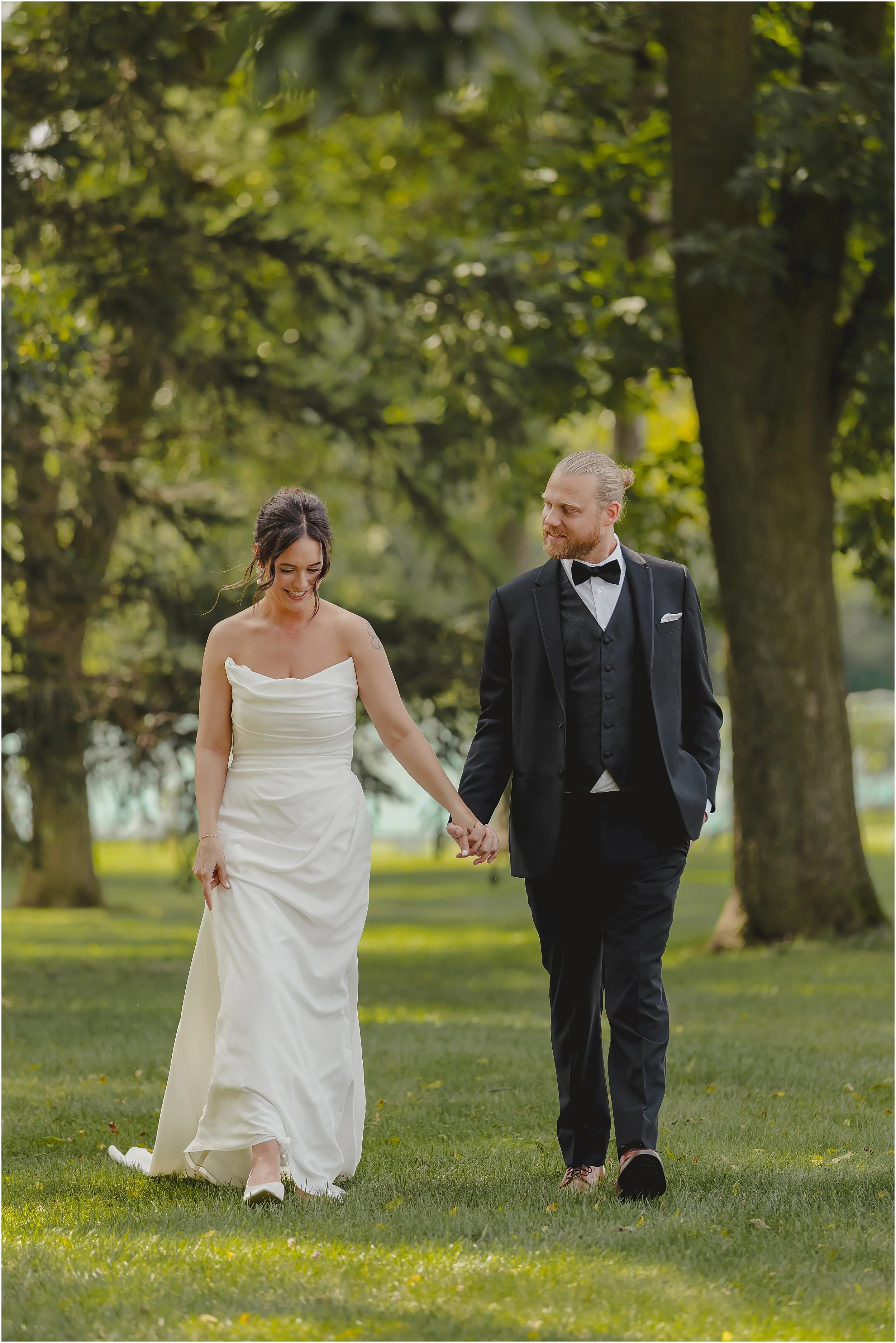 groom-looking-at-bride-walking-hand-in-hand-lush-green-trees.JPG