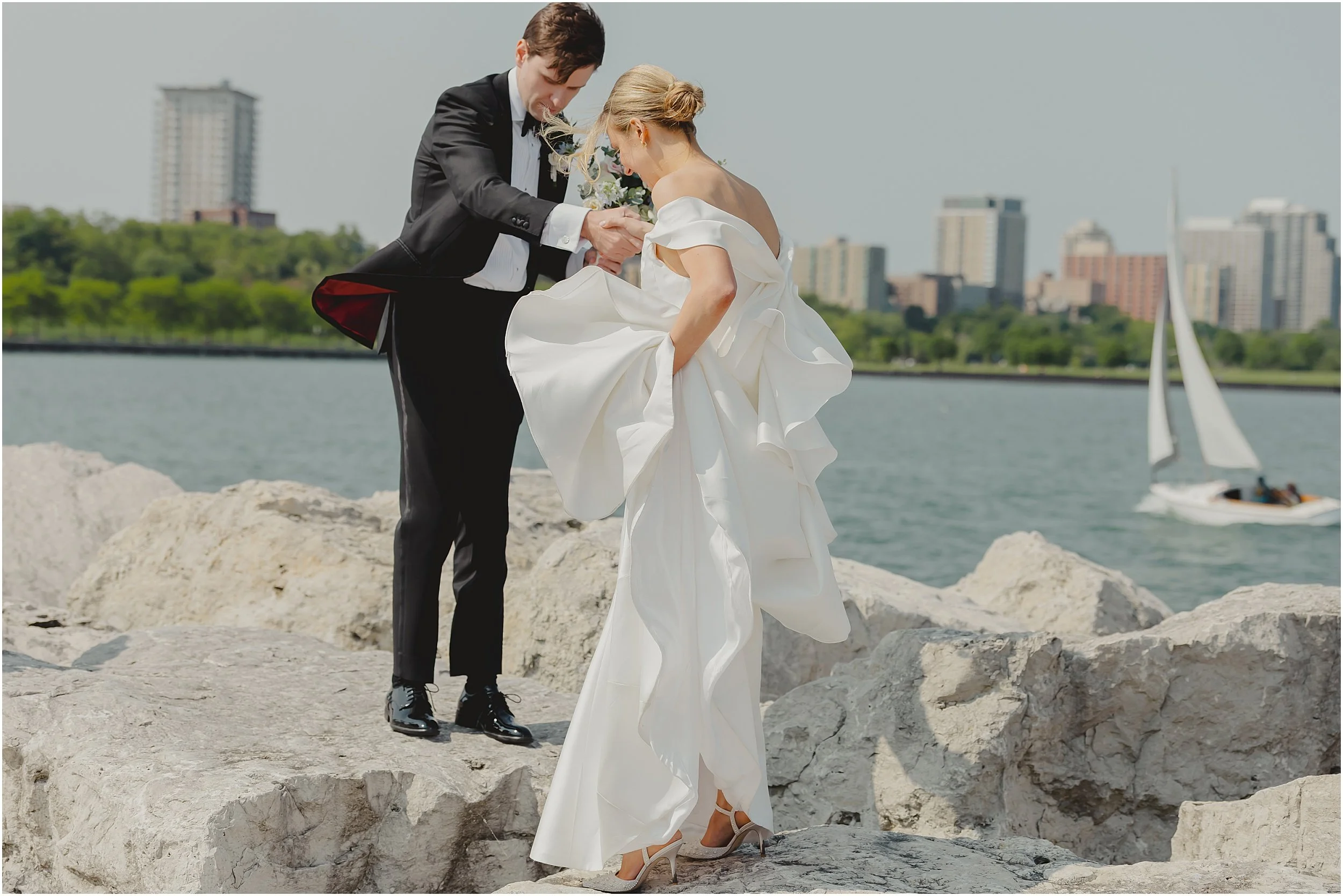 groom-helping-bride-onto-rock-by-lake-with-sailboat.JPG