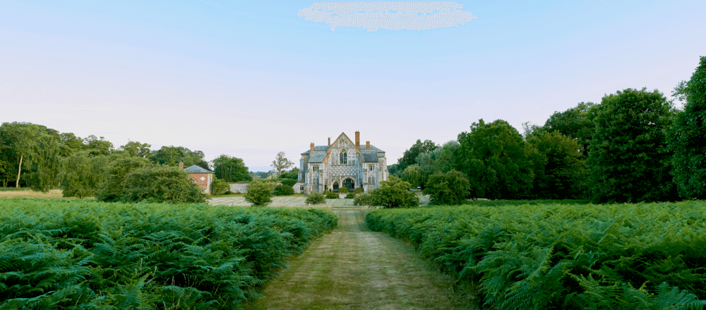 a view of suffolk wedding venue butley priory against a summer sky, with green bracken in the foreground