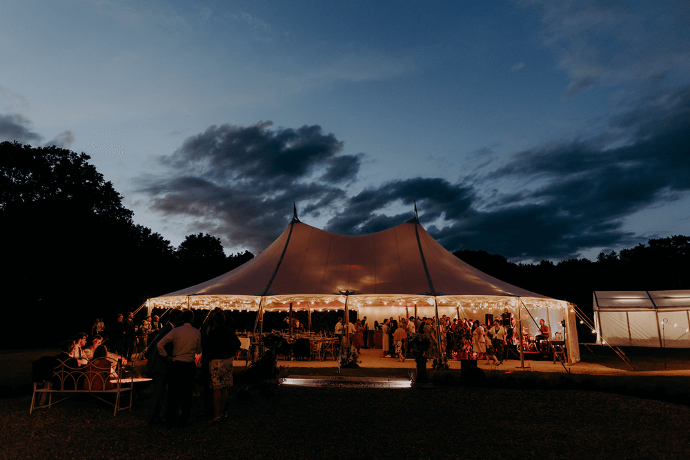a twilight scene of a marquee with warm glowing festoon lighting outside butley priory,