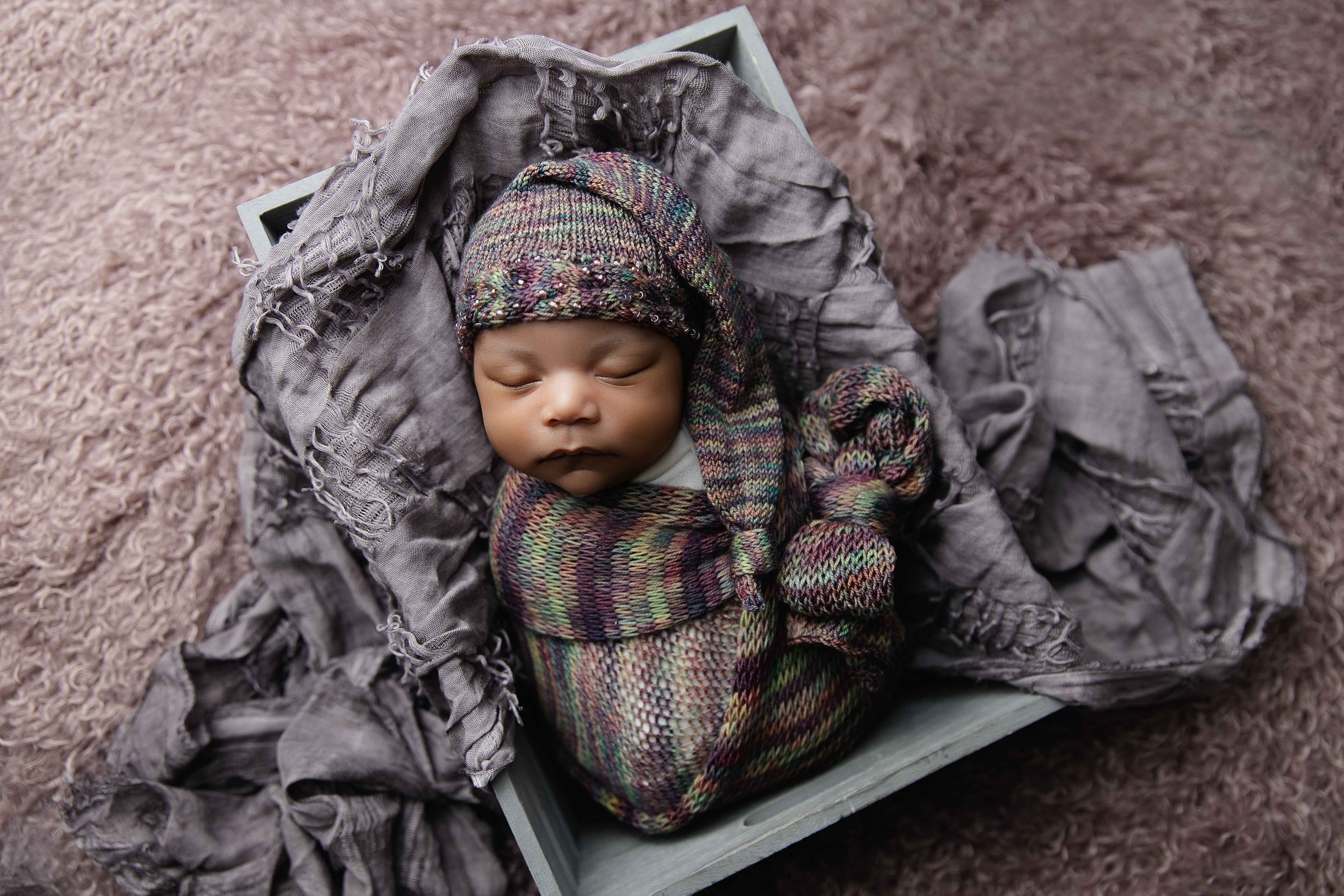 Newborn wrapped and posed in a crate grey, and mauve tones