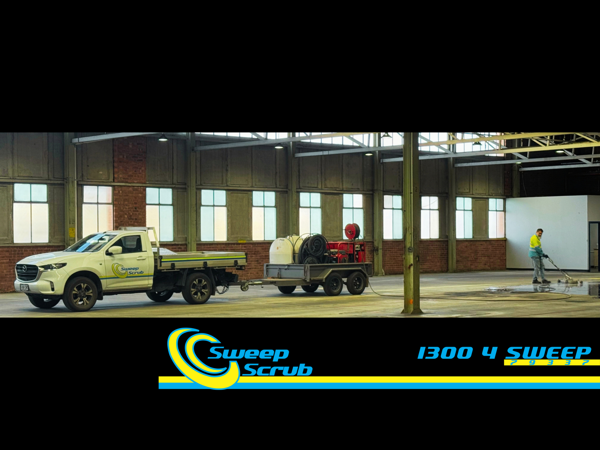 Inside an industrial building, a white Sweep Scrub service vehicle parked, with a person cleaning the floor nearby. The building has large windows, exposed brick and metal beams.