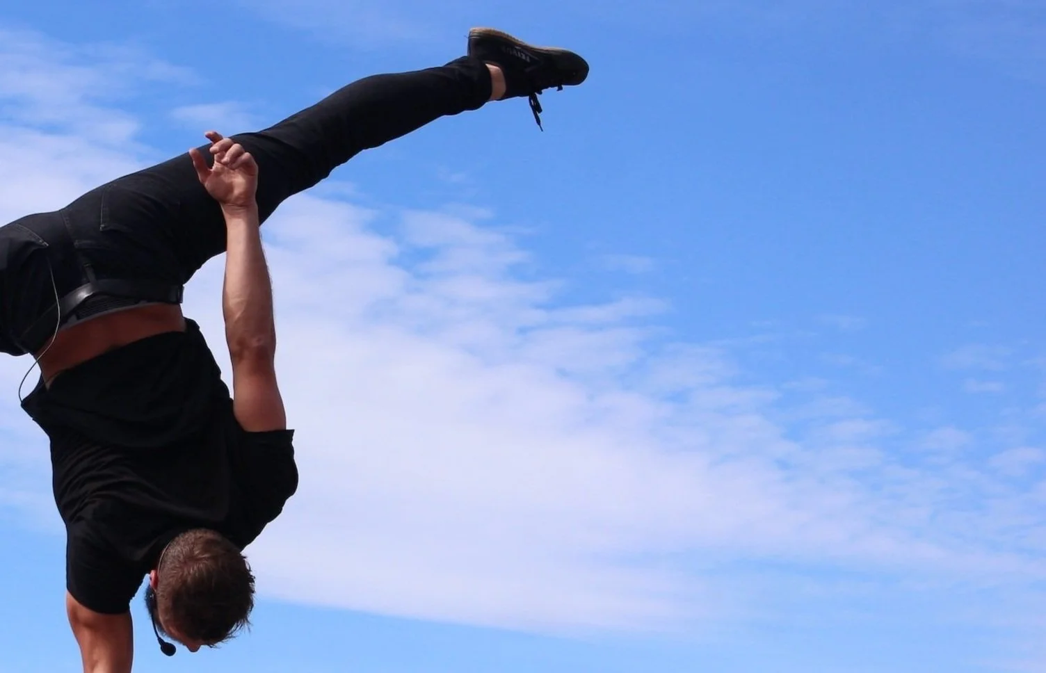 Person performing a handstand outdoors against a blue sky with clouds.