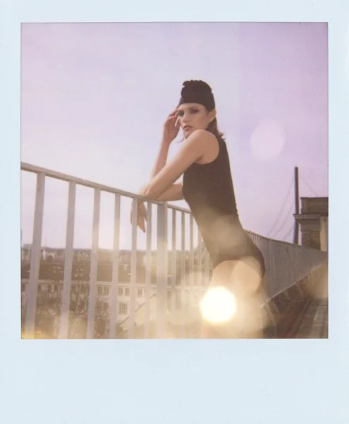 Junge Frau in einem Schwarzen Outfit auf einem Balkon bei Sonnenuntergang, mit Blick nach vorne.