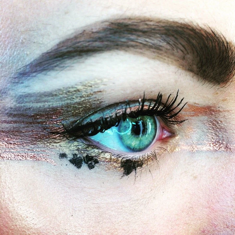 Nahaufnahme eines blauen Auges mit Make-up und Pinselstrichen in Gold und Schwarz