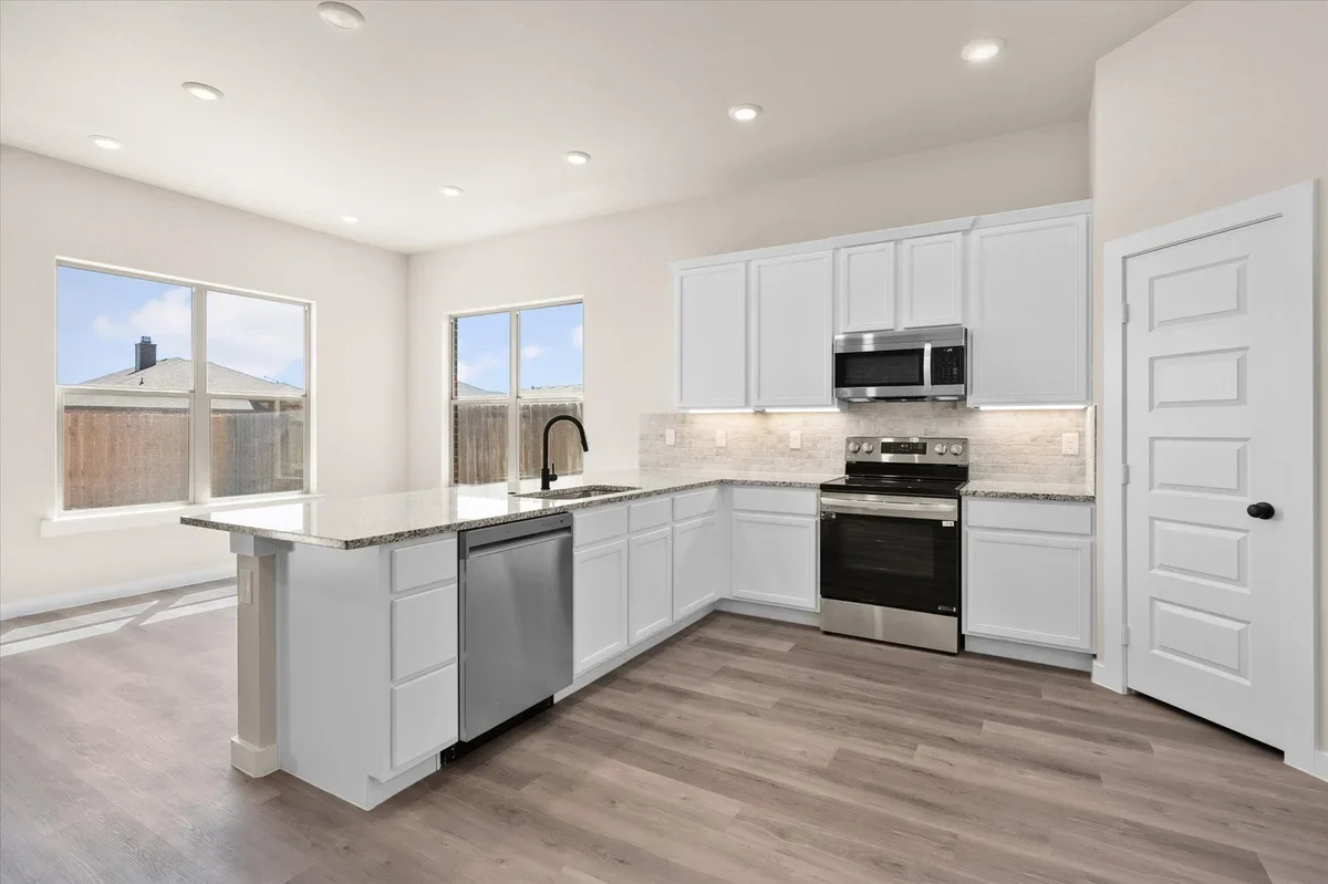 Empty modern kitchen with white cabinets, stainless steel appliances, granite countertops, and a light wood floor.