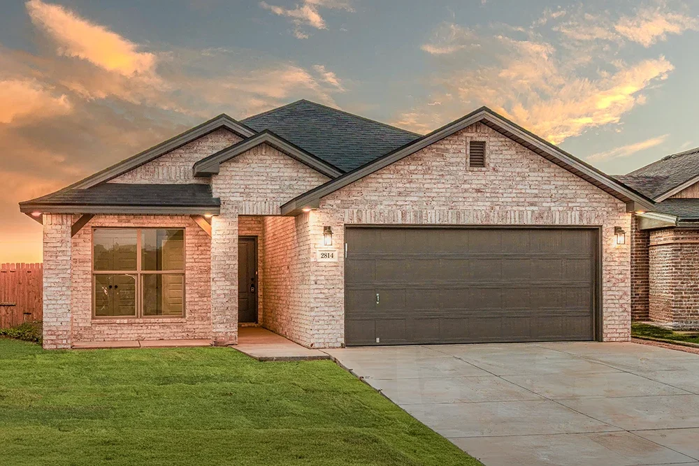 Exterior of a modern brick house with a green lawn and a two-car garage during sunset.