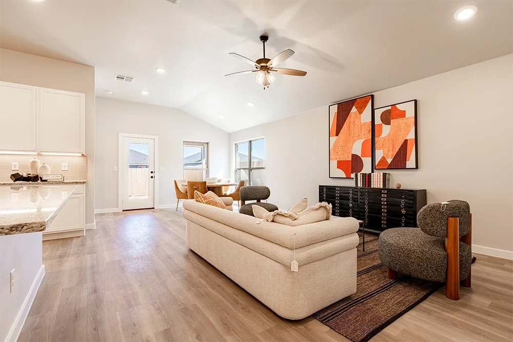 Living room with beige sofa, a round gray armchair, a black sideboard, and two abstract art pieces on the wall, in a bright, modern home interior.