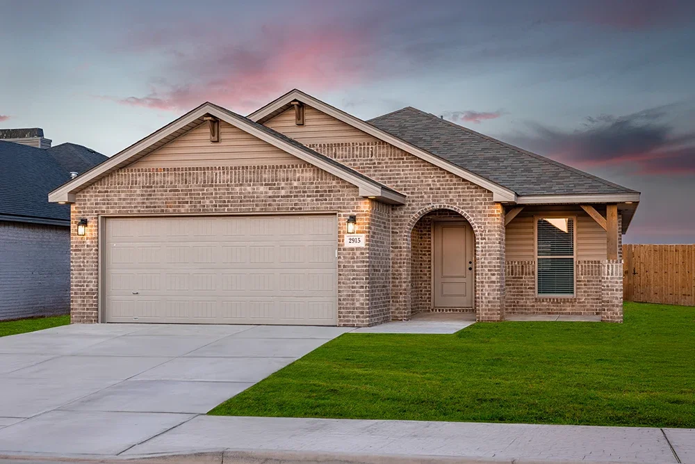 Front view of a new brick house with a two-car garage, a small front yard, and a front door, during cloudy sunset.